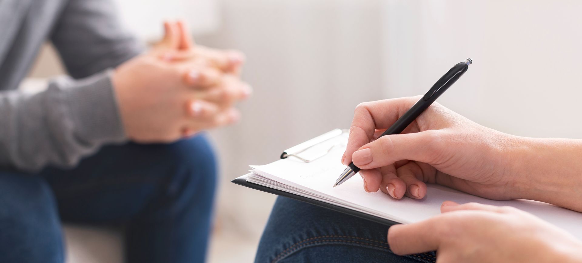 Person taking notes during a counseling session with a blurred seated listener in the background