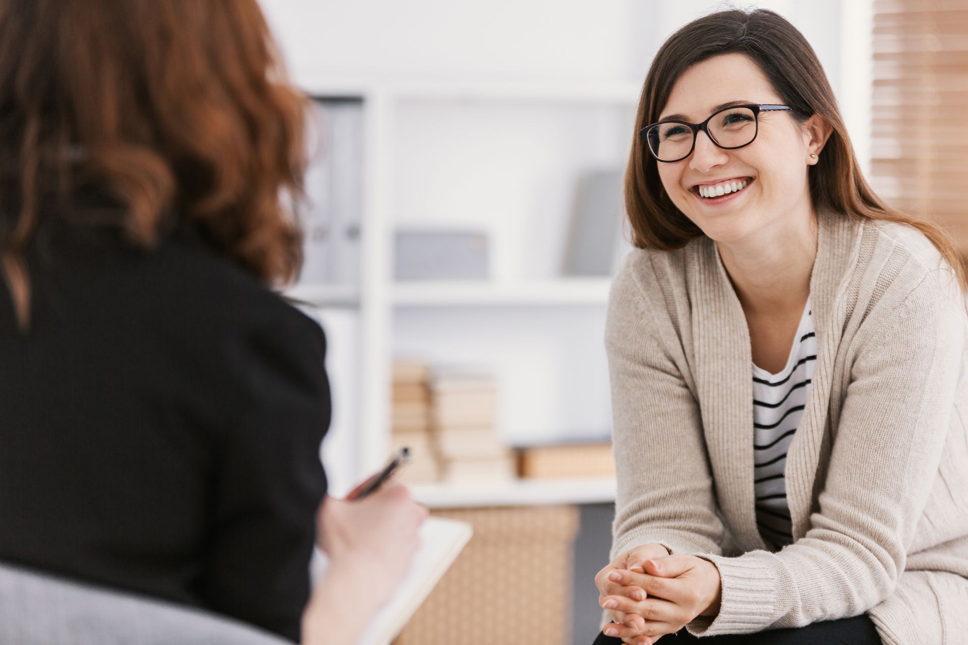 Two women in a bright office, smiling during a conversation across a table.