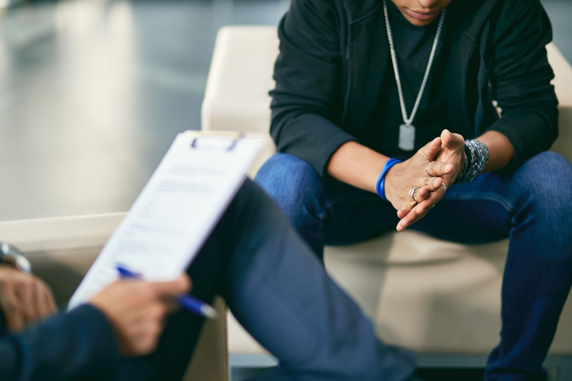 Two people in a counseling session, one holding a clipboard and the other seated with hands clasped.
