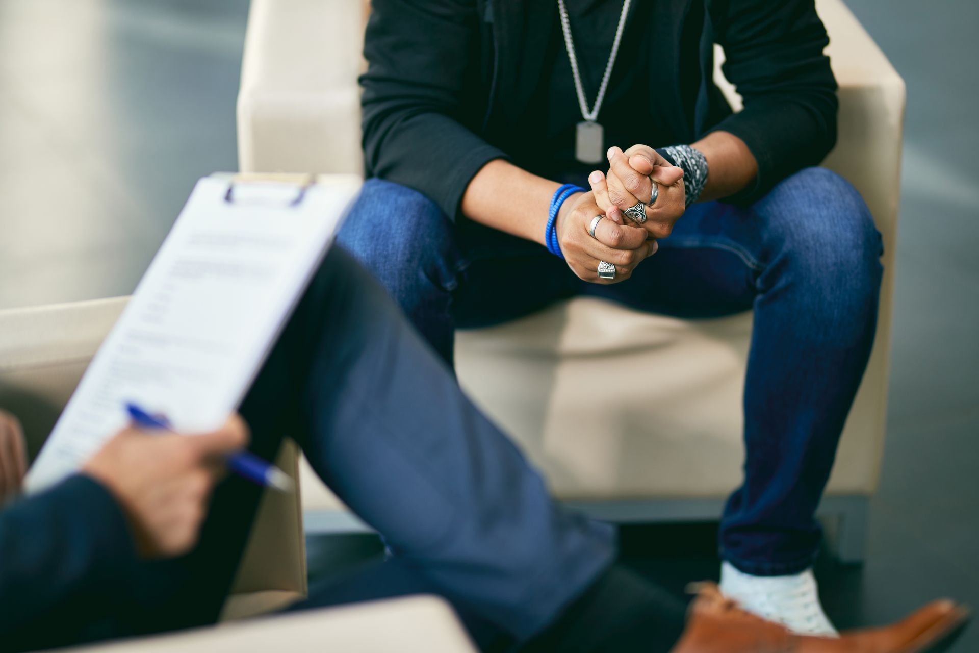 Person seated in a counseling session, hands clasped, with a clipboard in the foreground