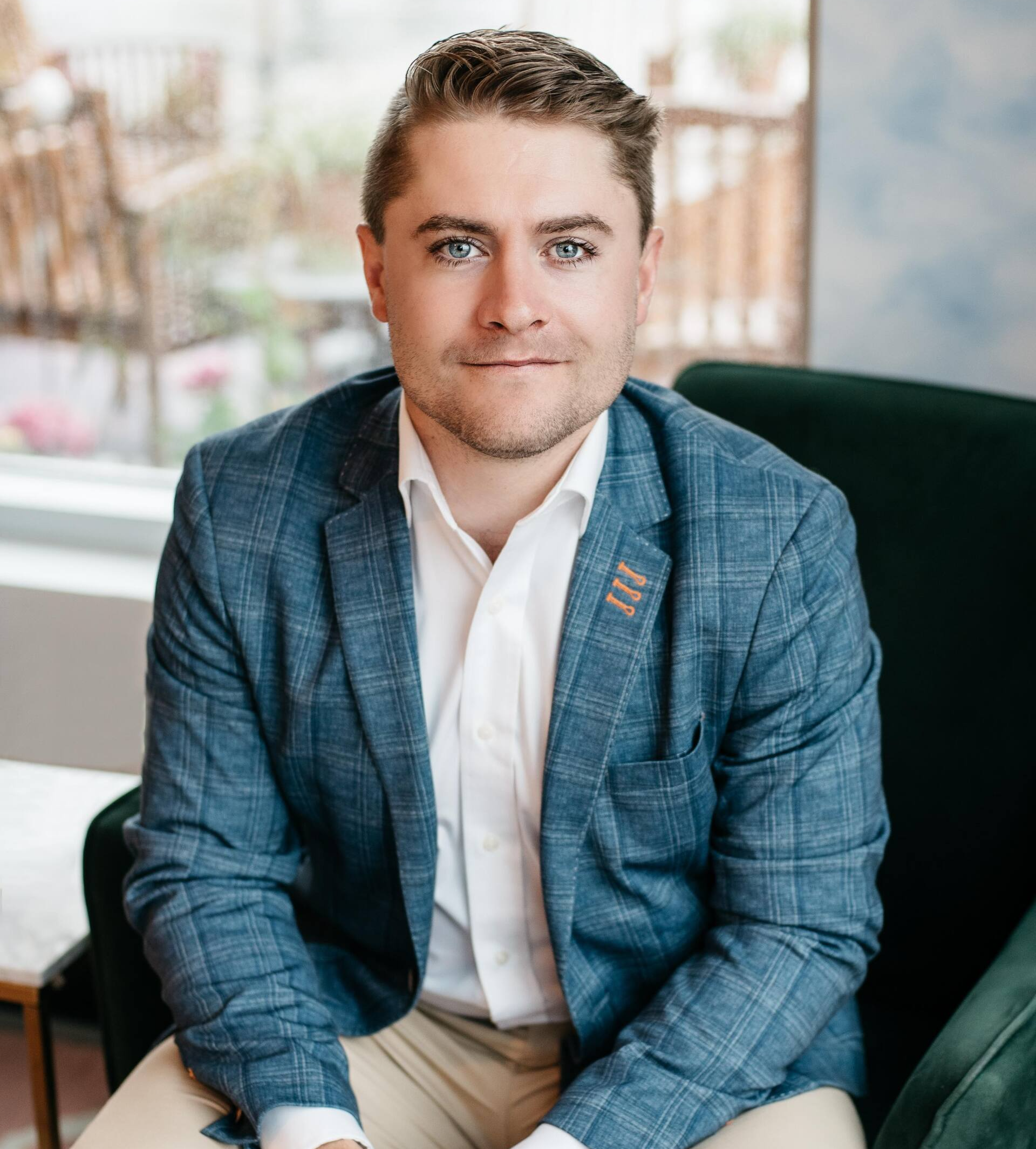 A man in a blue jacket and white shirt is sitting in a chair.