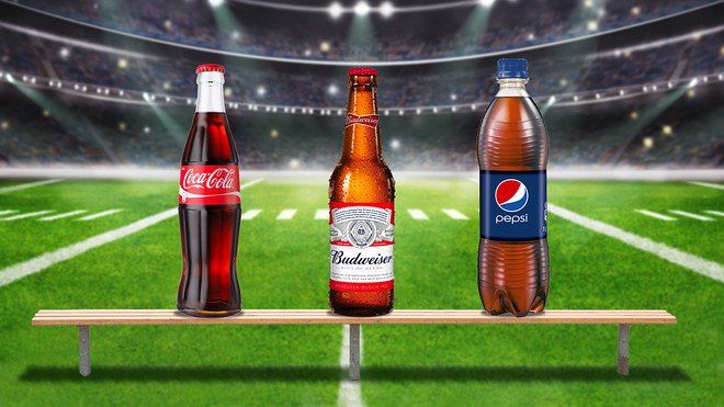 Three bottles of beer are sitting on a bench in front of a football field.