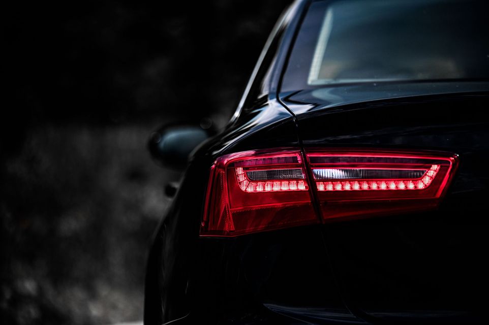 Rear of a black car with glowing red taillights in a dark setting