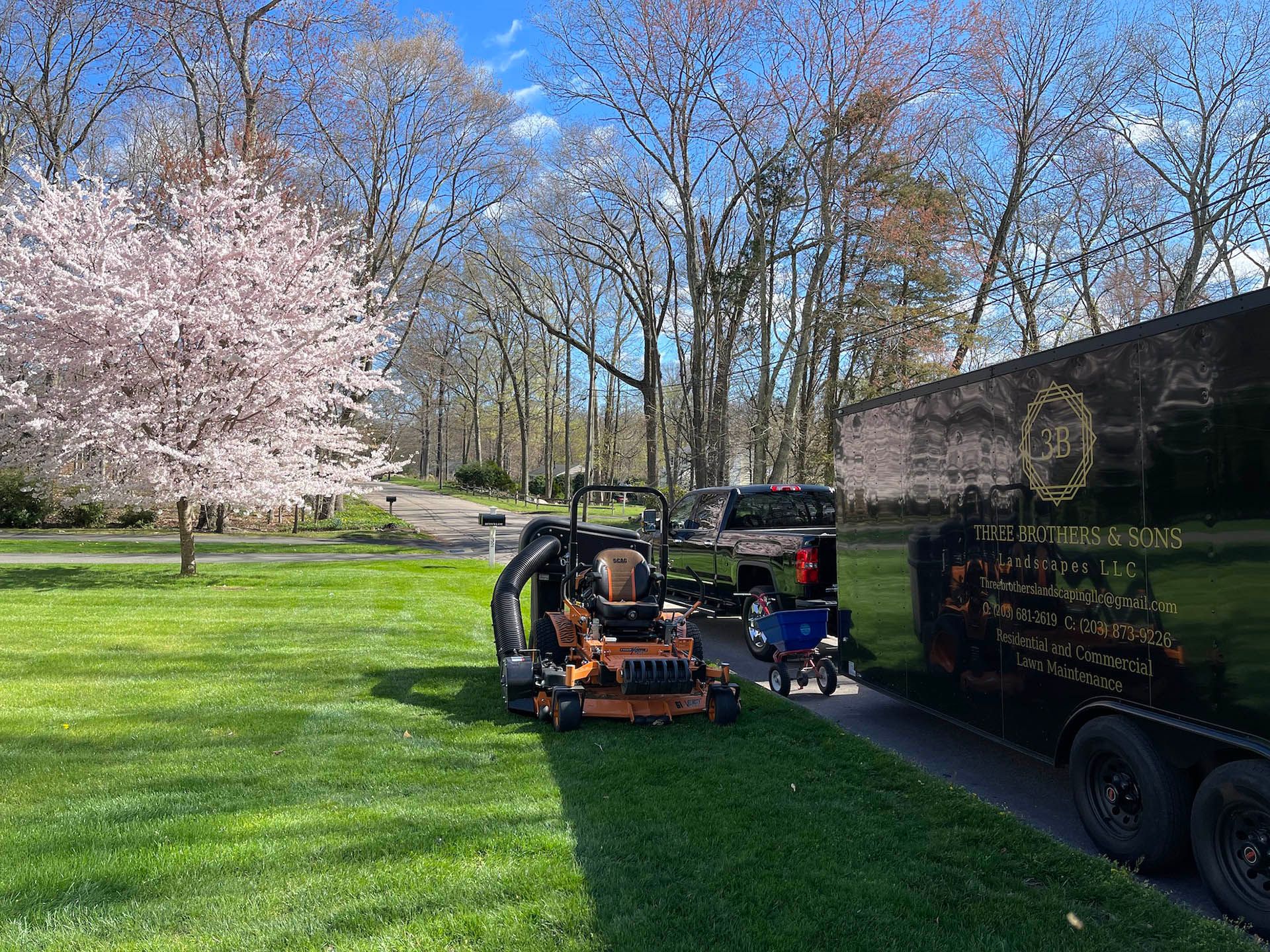 A lawn mower is parked next to a trailer in a park.