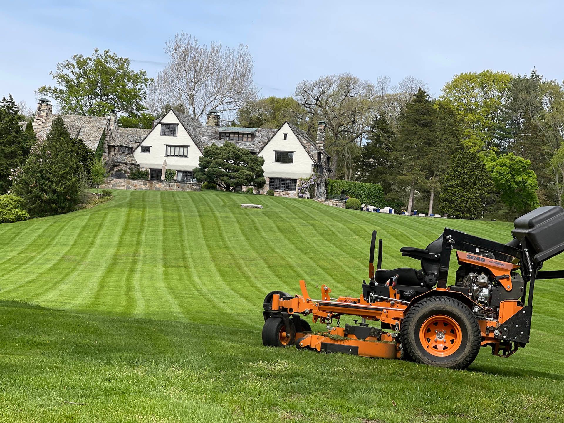 A lawn mower is cutting a lush green lawn in front of a house.