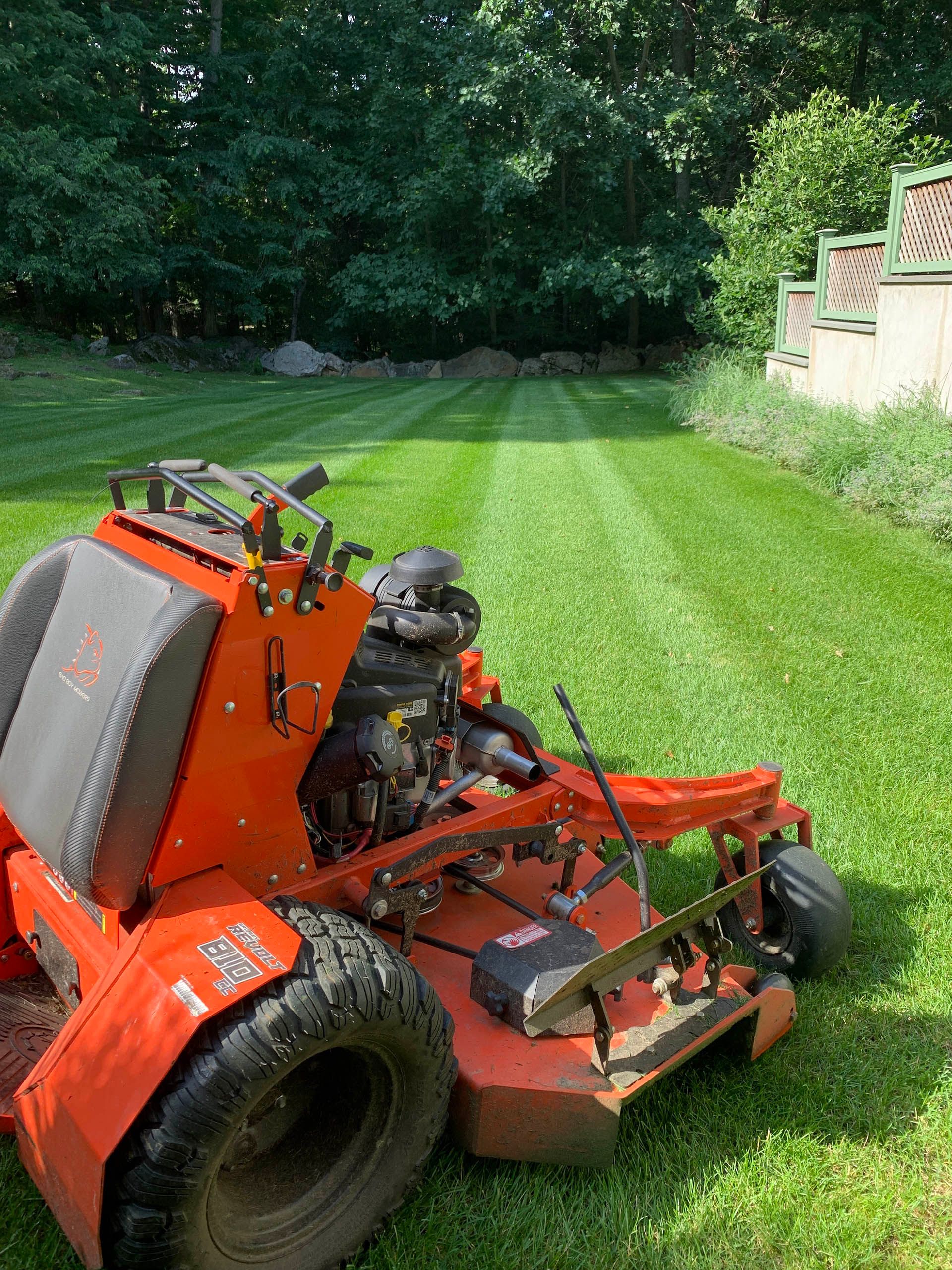 An orange lawn mower is sitting on top of a lush green lawn.