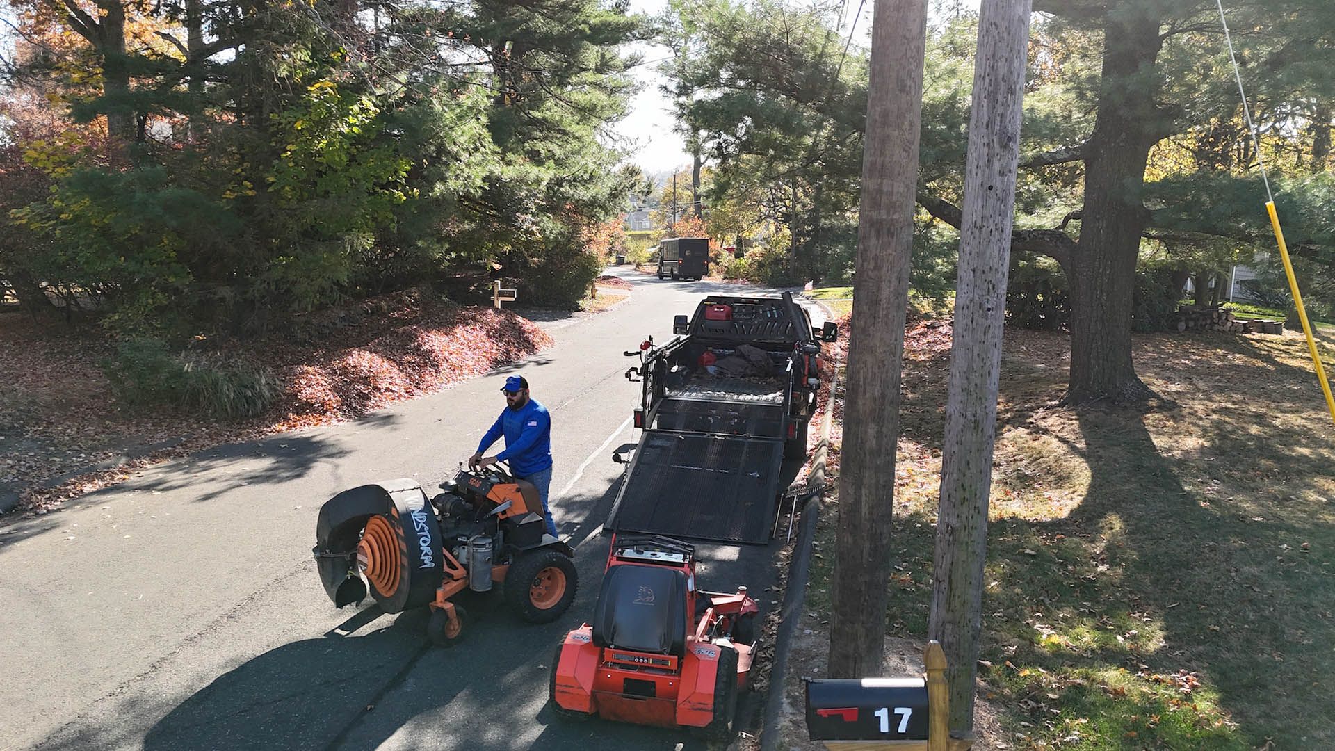 A man is driving an atv down a road next to a mailbox with the number 17 on it