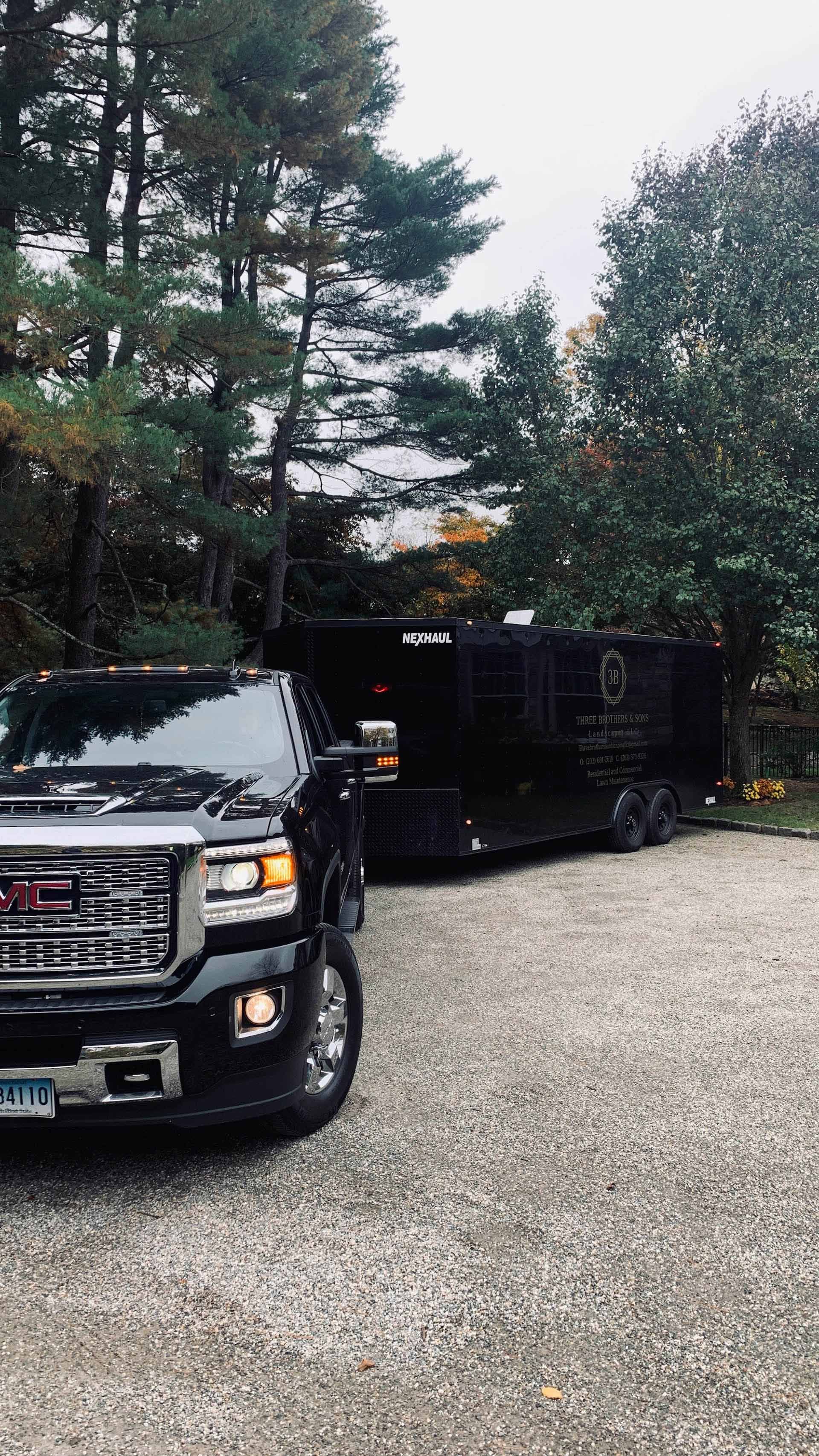 A black truck is parked in a gravel driveway next to a trailer.