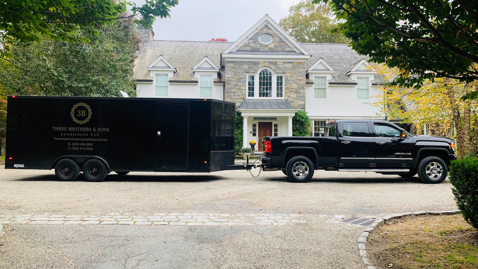 A black truck with a trailer attached to it is parked in front of a large house.