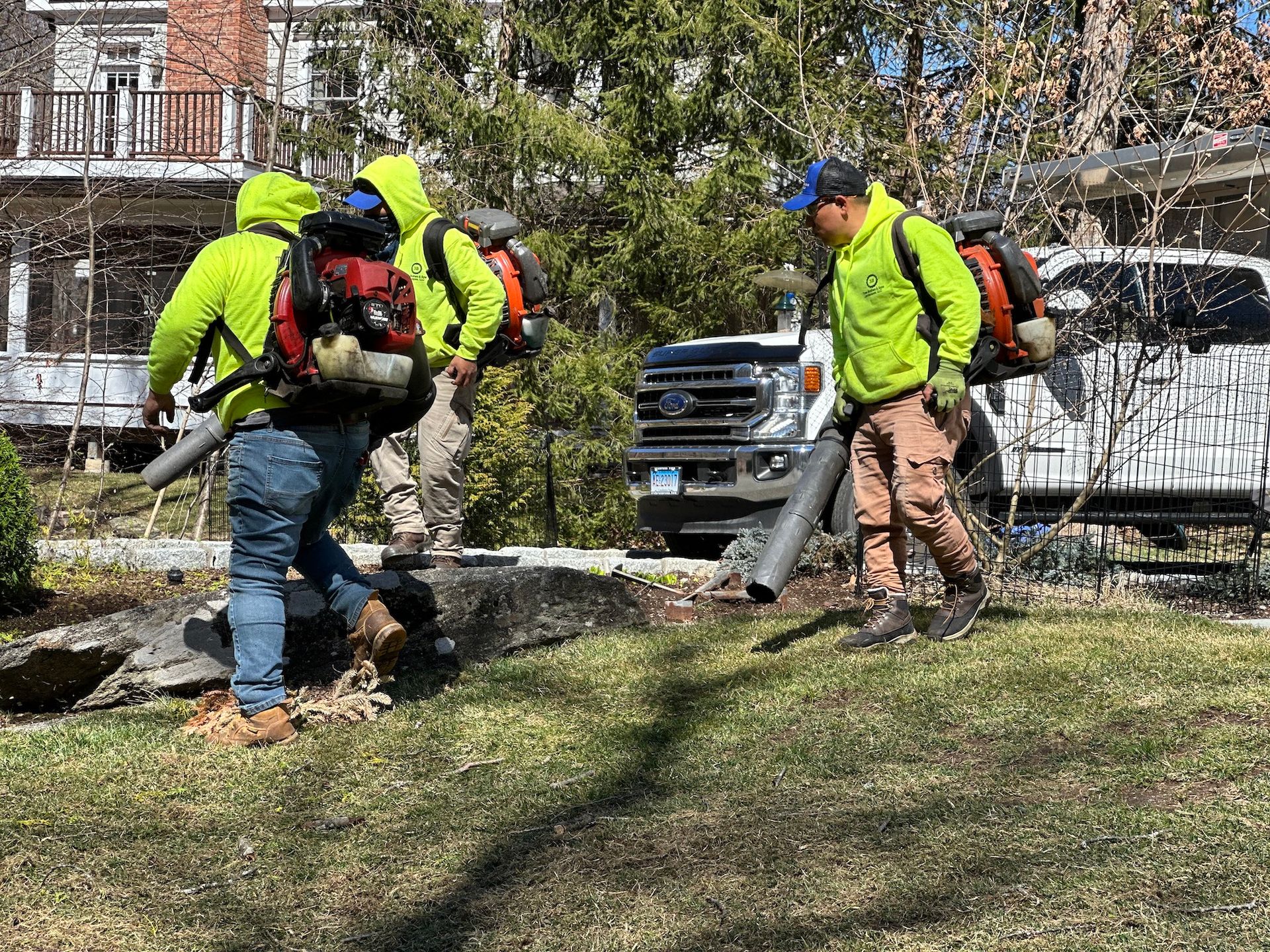 A group of men are blowing leaves in a yard.