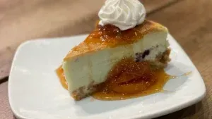 A slice of cheesecake with whipped cream and jam on a white plate.
