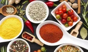 A variety of spices and vegetables in bowls and spoons on a table.