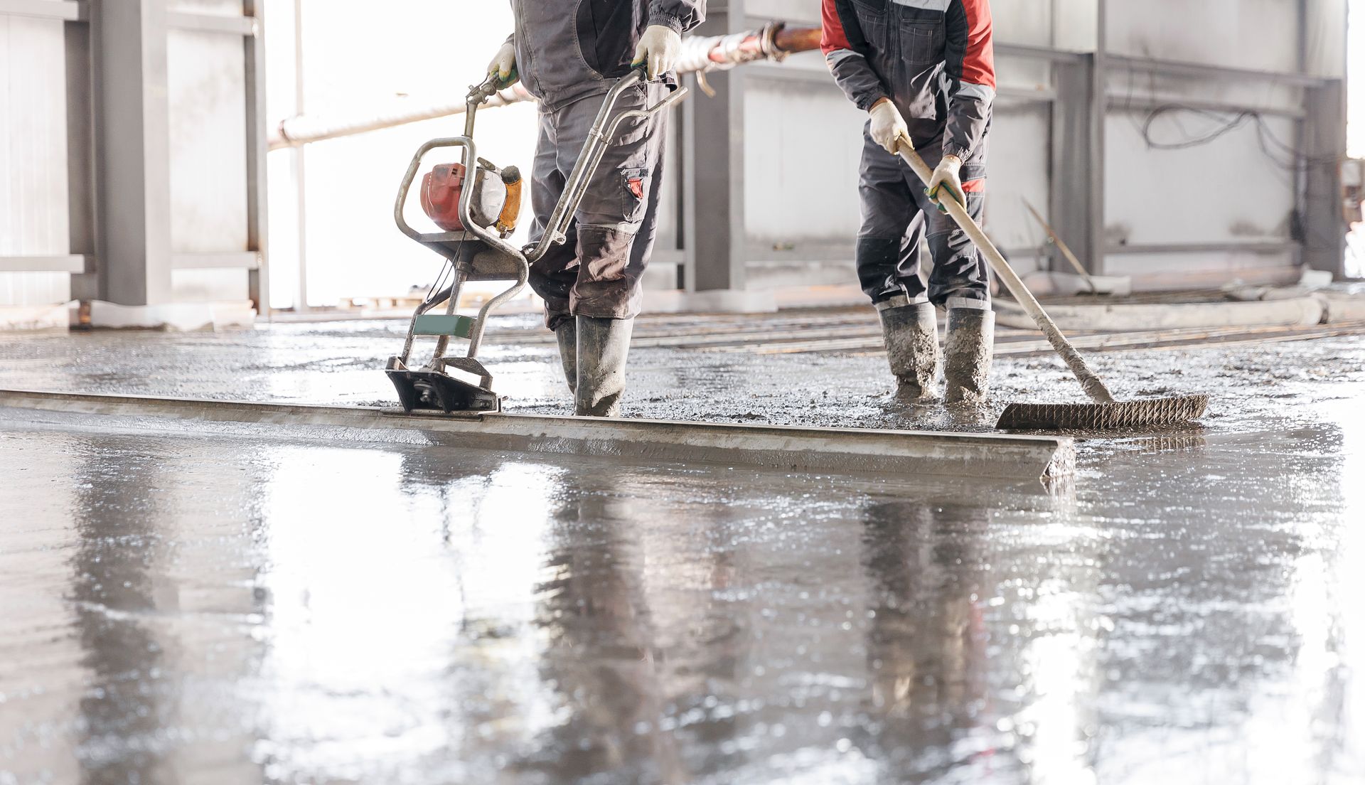 Two workers smoothing and finishing a freshly poured concrete slab.