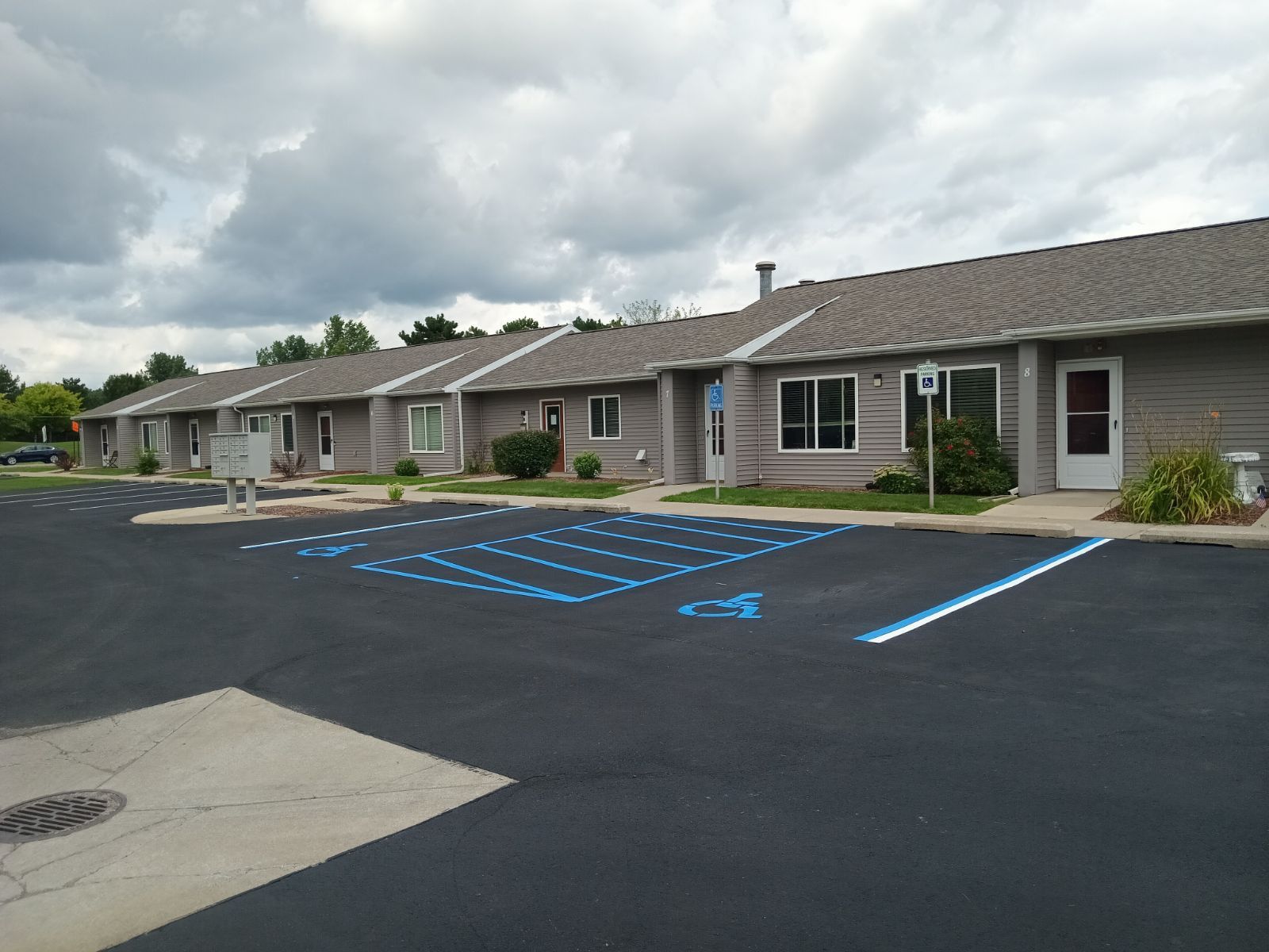Newly paved black asphalt parking lot next to a gray concrete sidewalk; Black Jack Asphalt & Concrete logo. Newly paved black asphalt parking lot next to a gray concrete sidewalk; Black Jack Asphalt & Concrete logo.