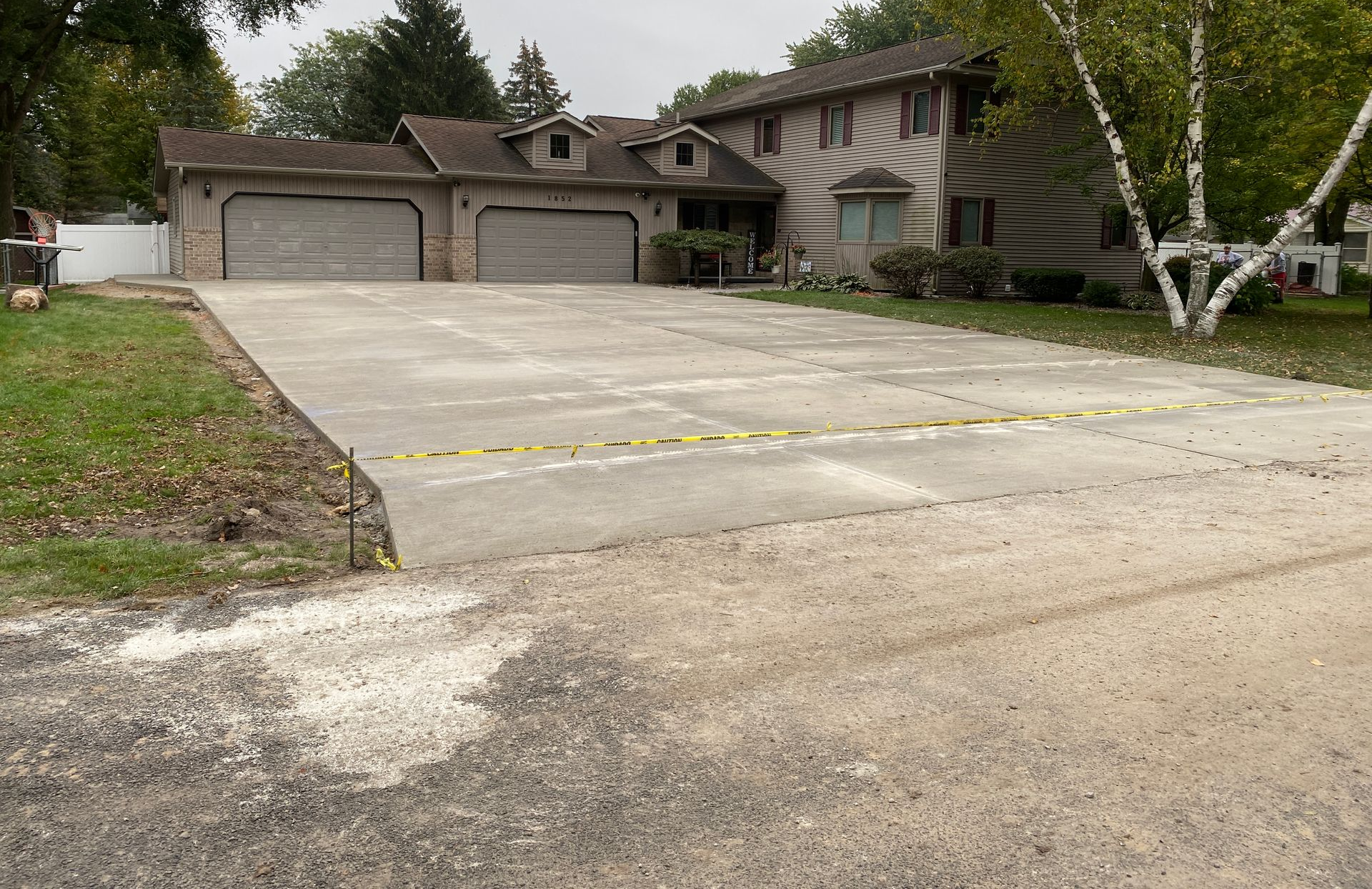 Black asphalt driveway curves through a grassy lawn with trees, under a bright, cloudy sky. Black asphalt driveway curves through a grassy lawn with trees, under a bright, cloudy sky.