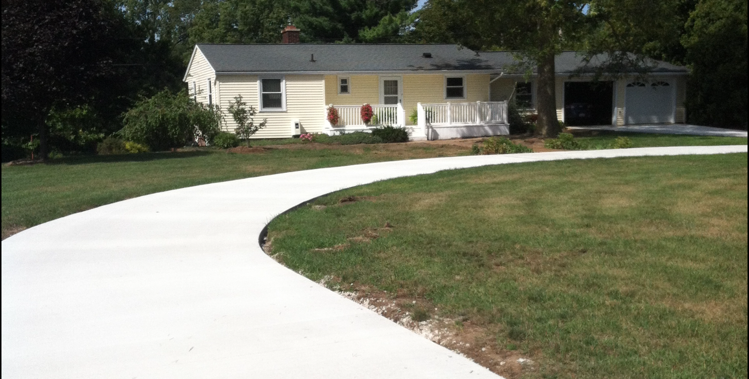 Curving concrete driveway leads to a light yellow house with white porch and attached garage. Curving concrete driveway leads to a light yellow house with white porch and attached garage.