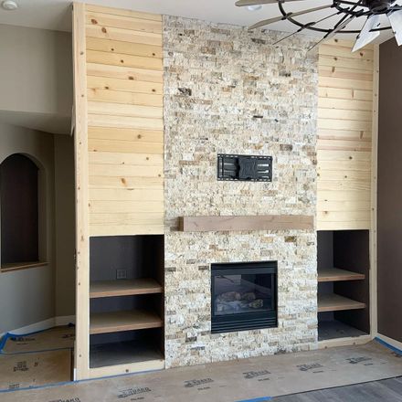 A living room with a stone fireplace and wood paneling.