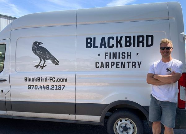 A man is standing in front of a blackbird finish carpentry van.