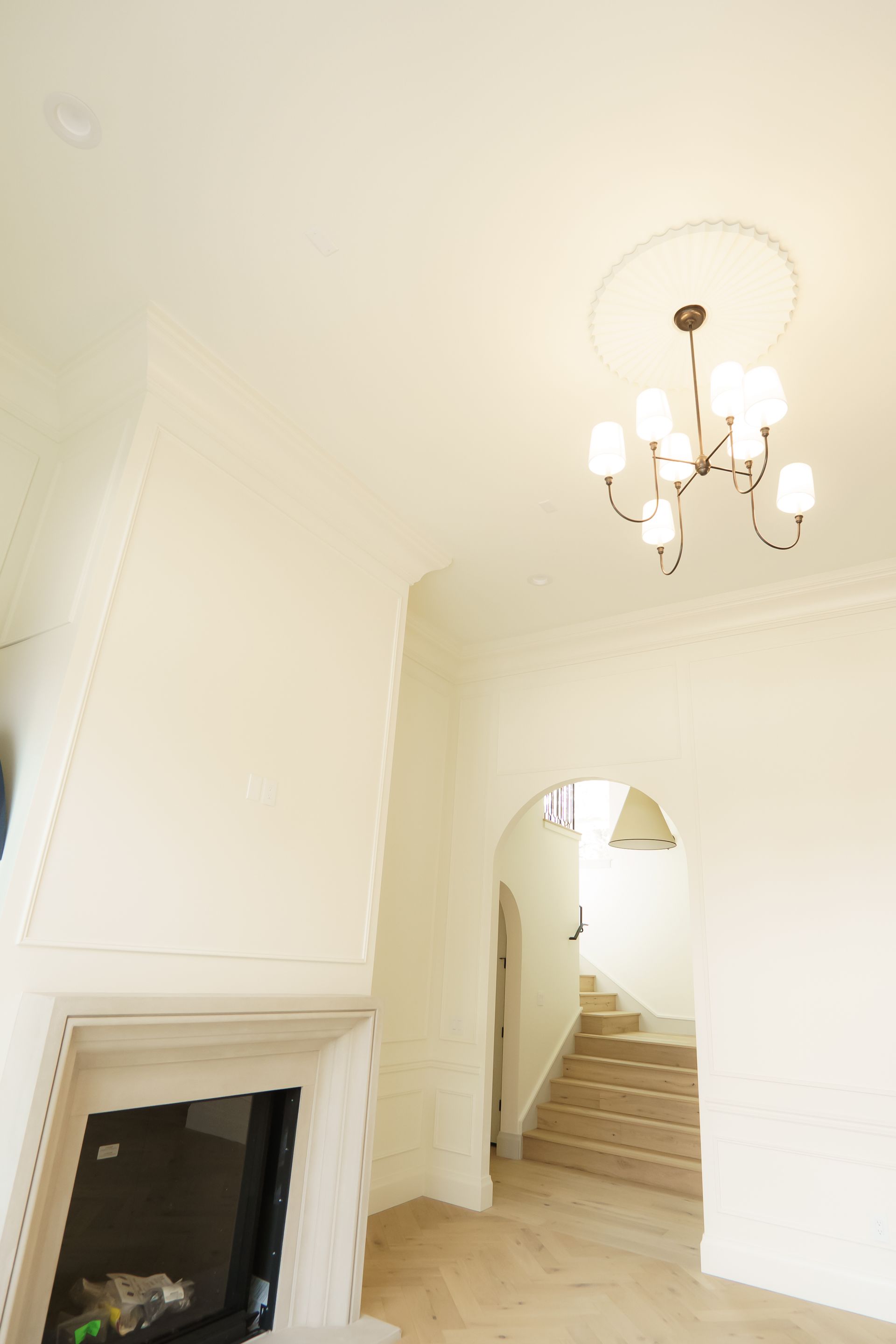 A living room with a fireplace and stairs and a chandelier hanging from the ceiling