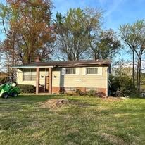 House with green lawn, trees, and small vehicle. Overcast sky.