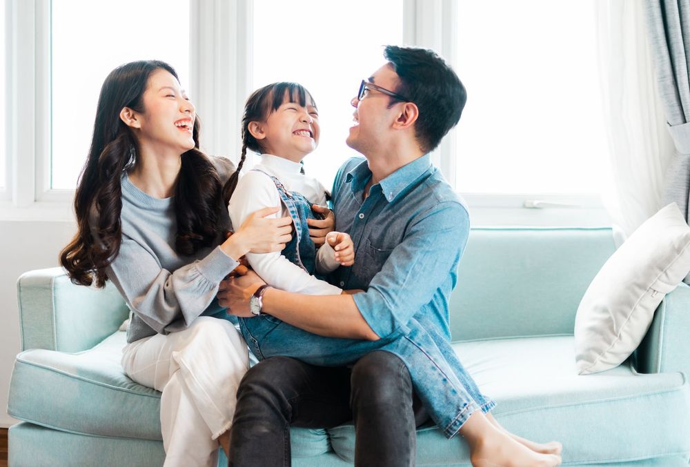 A family is sitting on a couch holding a little girl.