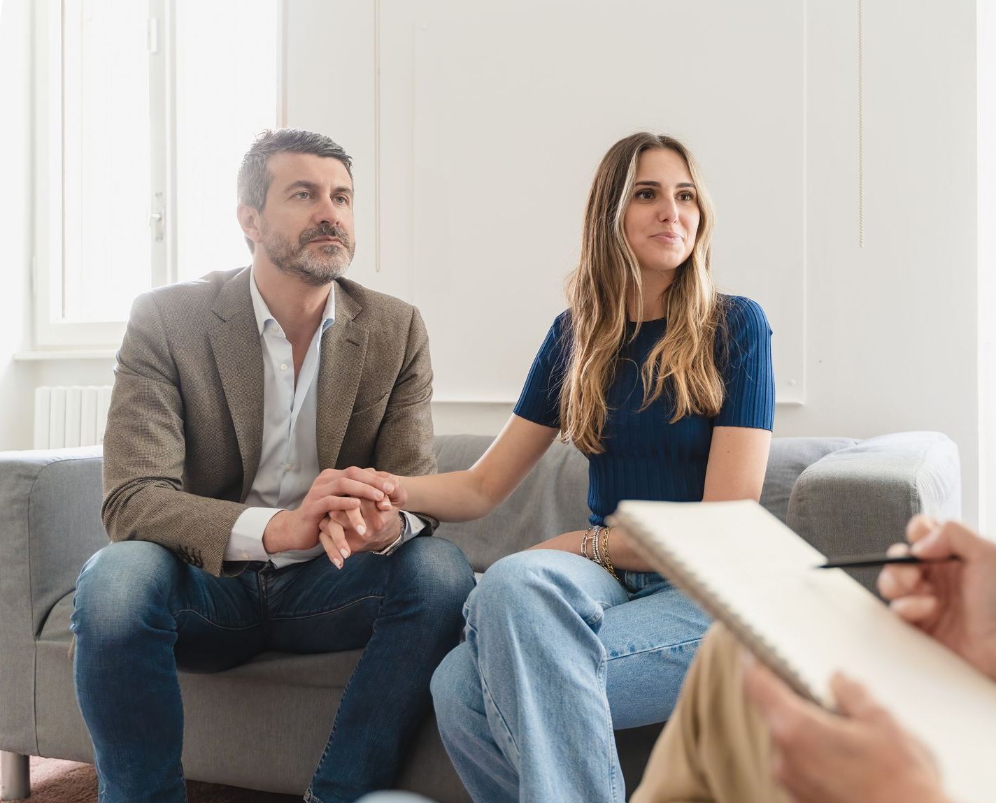 A man and a woman are sitting on a couch holding hands.