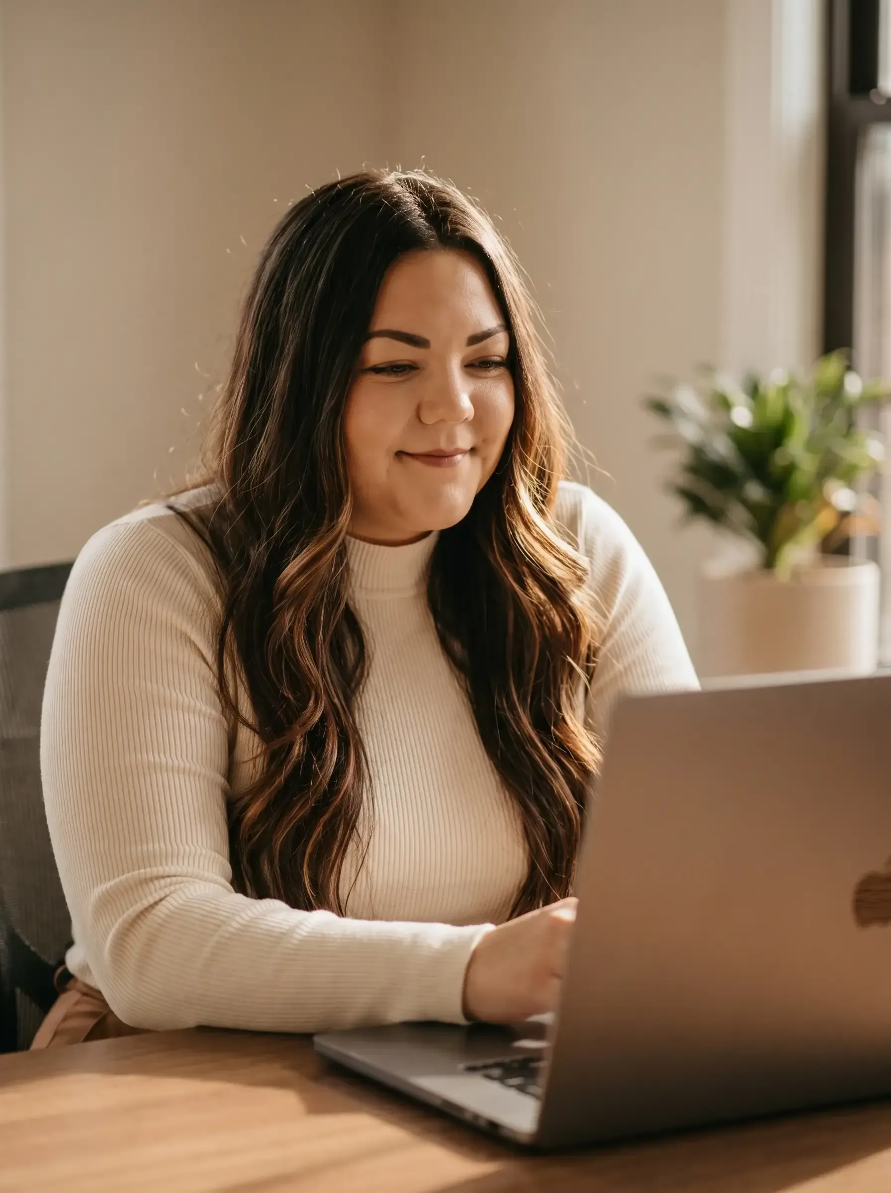 Woman smiling at a laptop on a wooden table in a bright room