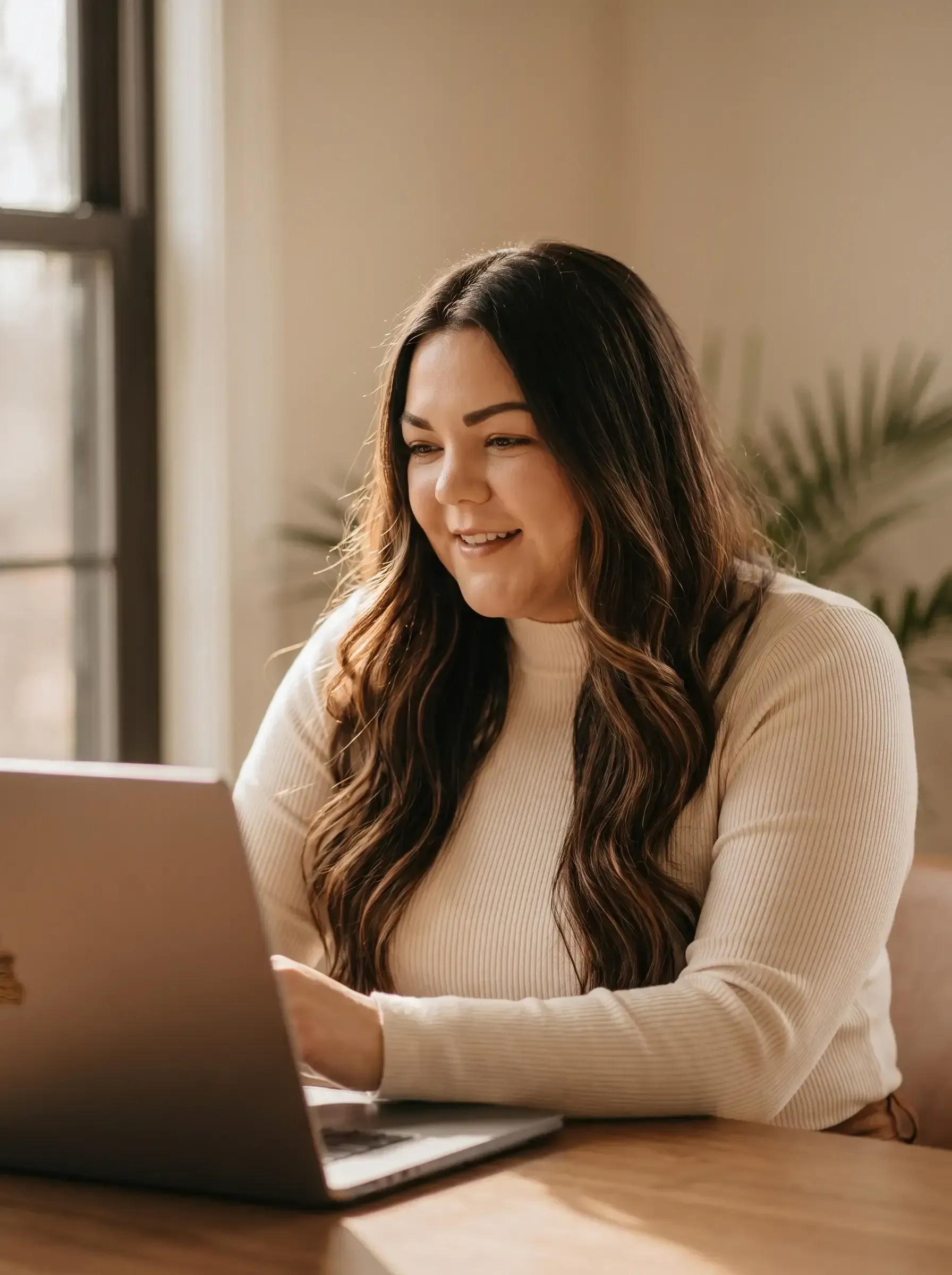 Person smiling and typing on a laptop at a table in a bright room