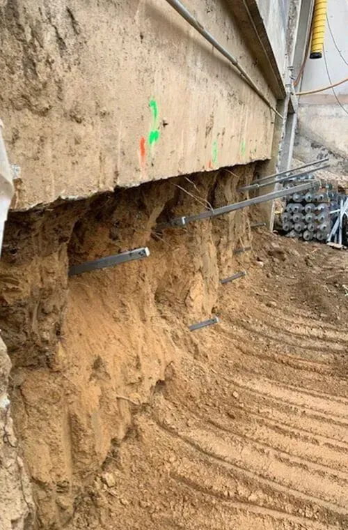 Construction site. Exposed concrete beam with metal rods inserted into the soil. Earth has been excavated below the beam.