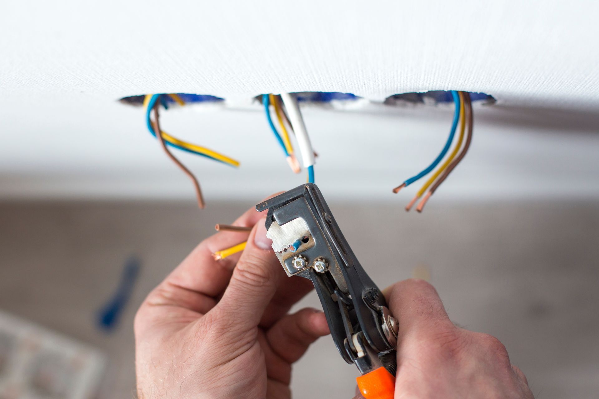 Electrician stripping wires from ceiling electrical box using a wire tool.