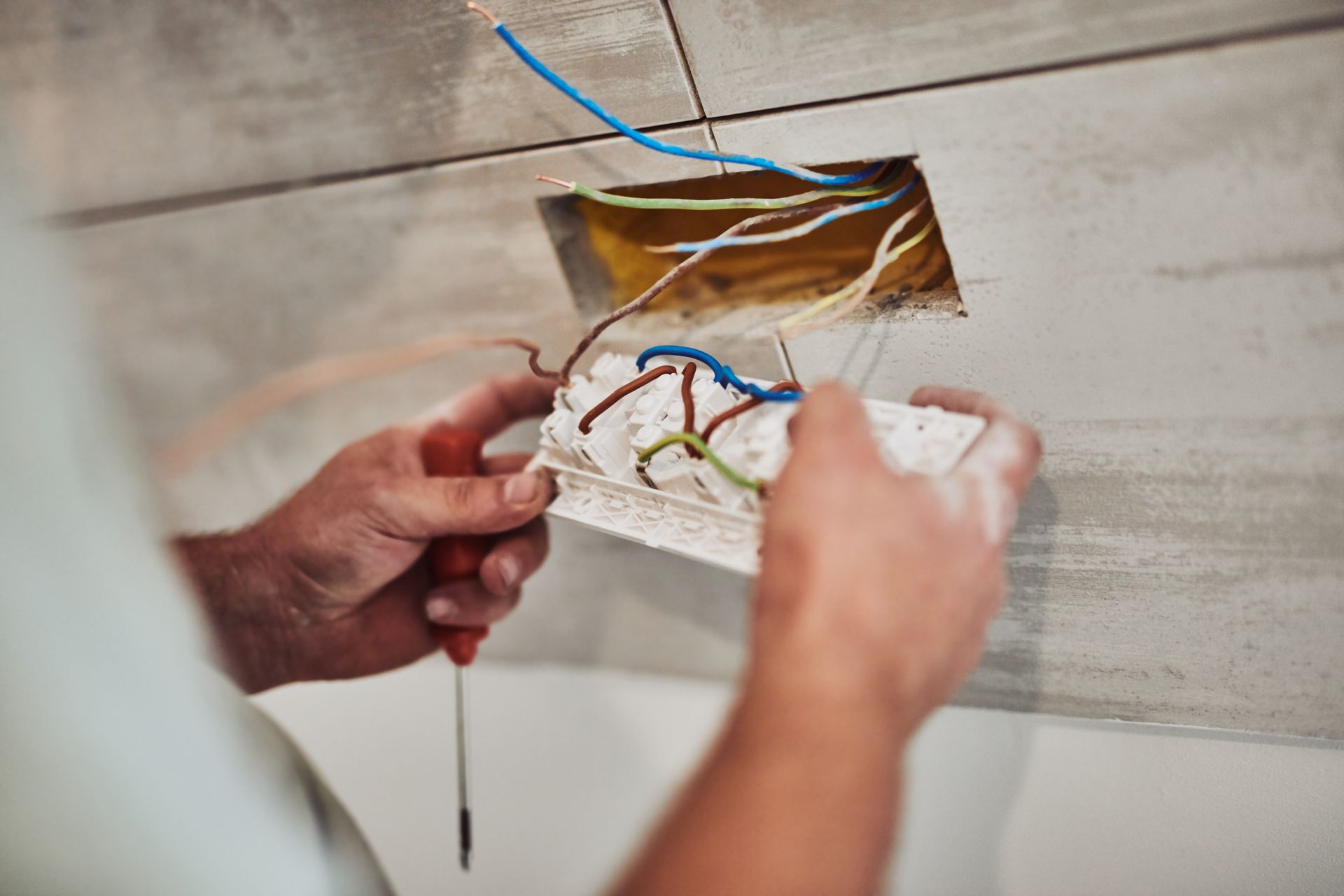 Hands connecting electrical wires in wall box opening on tiled wall. Hands connecting electrical wires in wall box opening on tiled wall.
