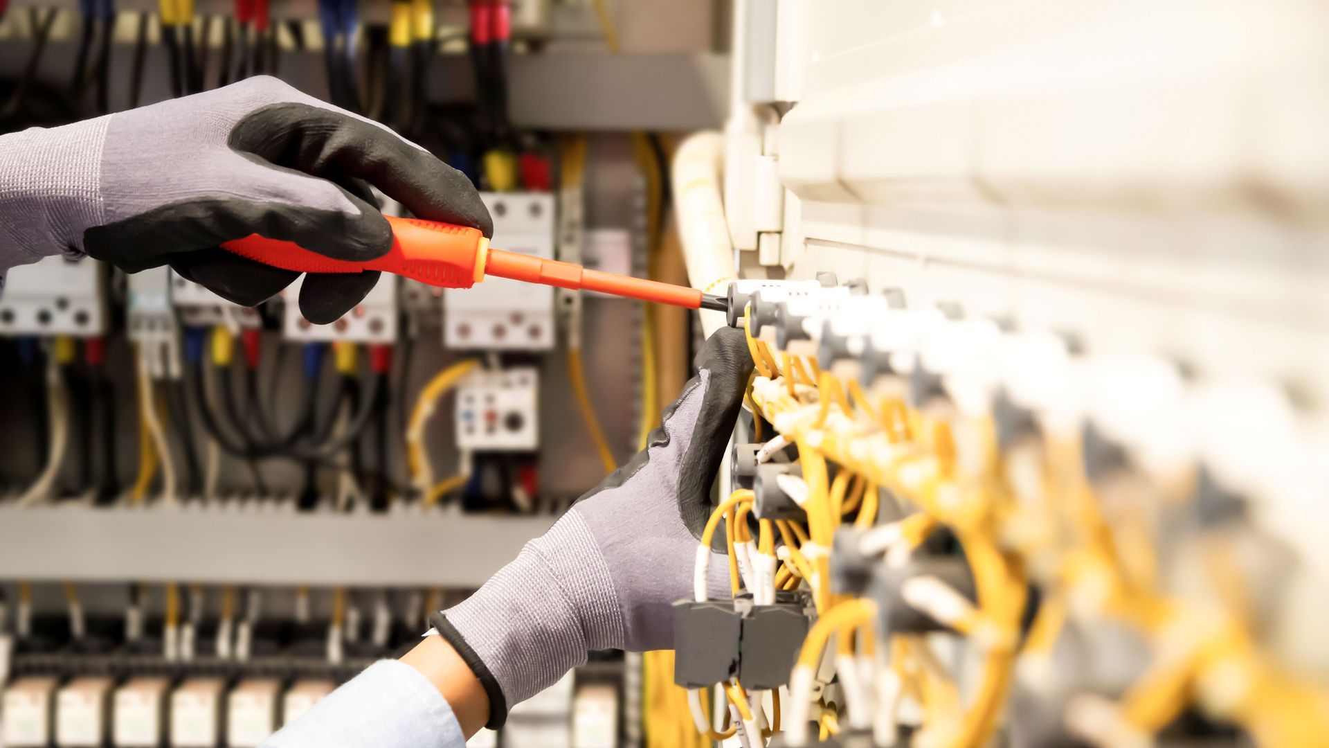 Gloved electrician performing electrical repairs on a wired control panel.