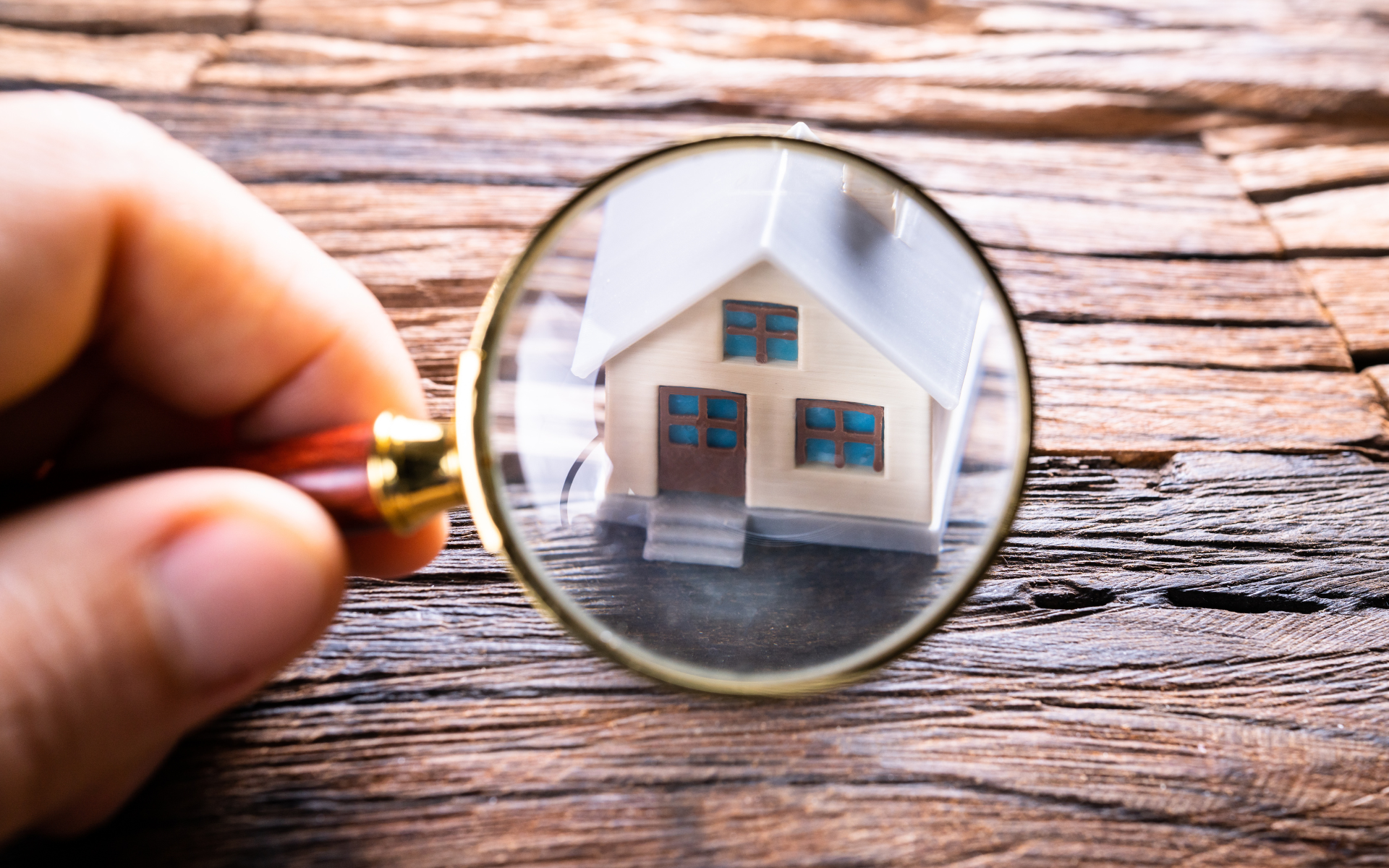 Hand holding magnifying glass over a house, highlighting home inspection or property search