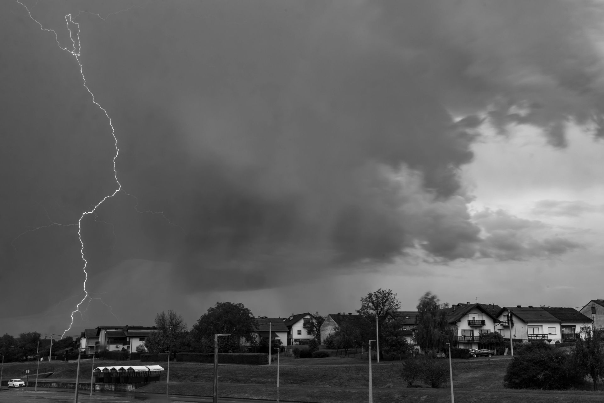 Lightning striking over a suburban neighborhood under dark storm clouds.