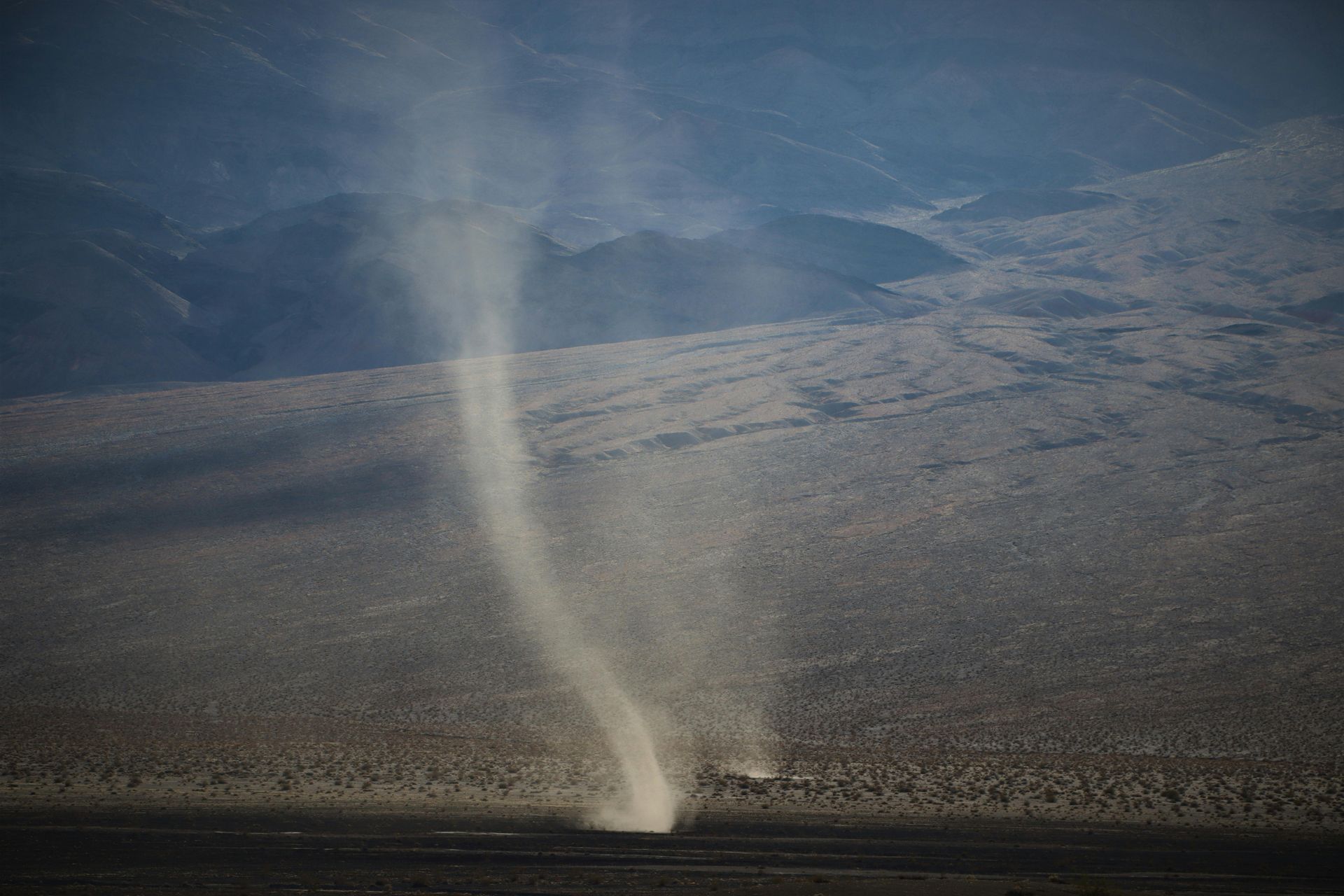Dust devil spiraling across a barren desert landscape with mountains in the distance