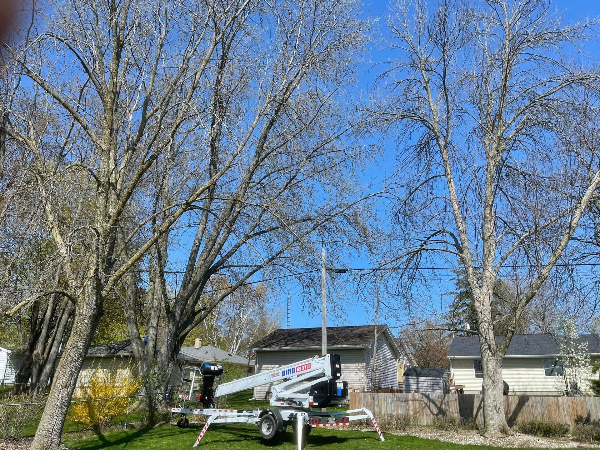 White helicopter parked in a yard beside houses and leafless trees under a blue sky