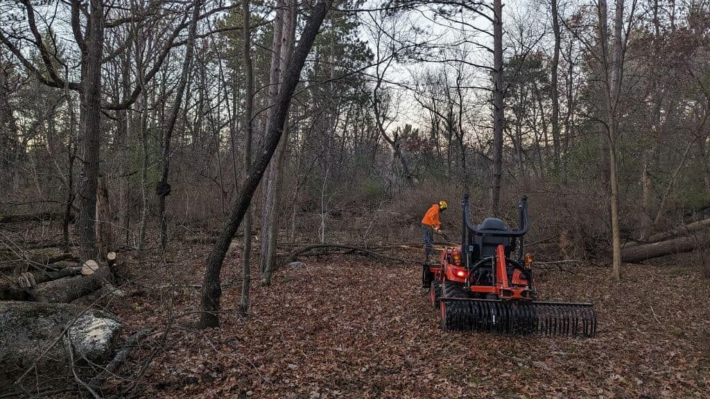 Orange tractor clearing leaves in a wooded area in autumn