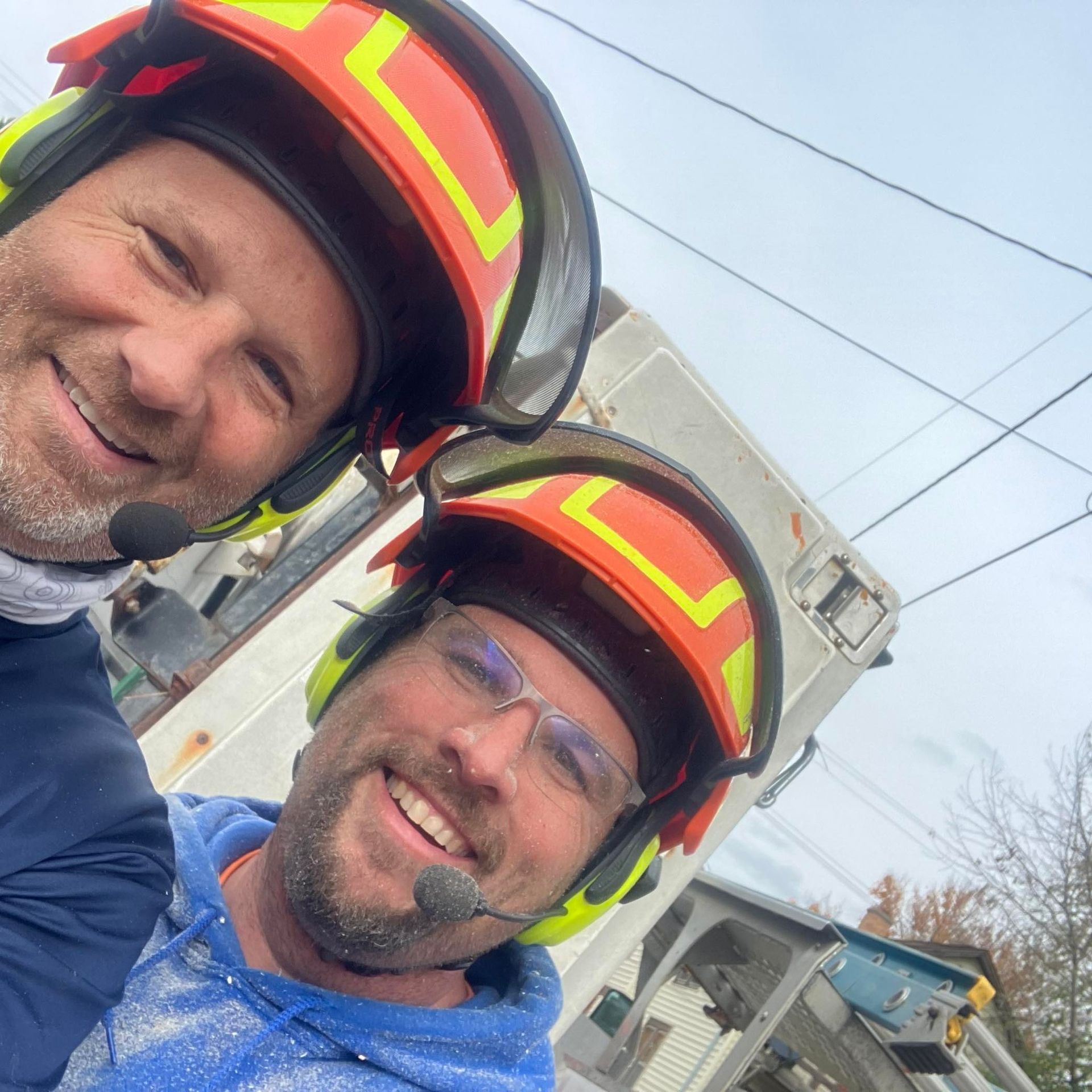 Two workers in safety helmets smiling beside a utility truck outdoors