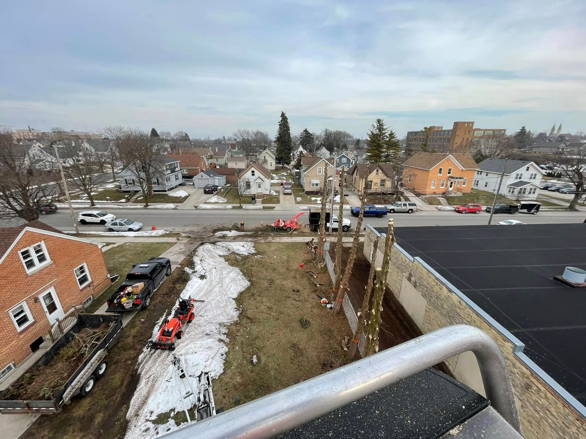 Rooftop view of a snowy neighborhood with houses, parked cars, and a street below.