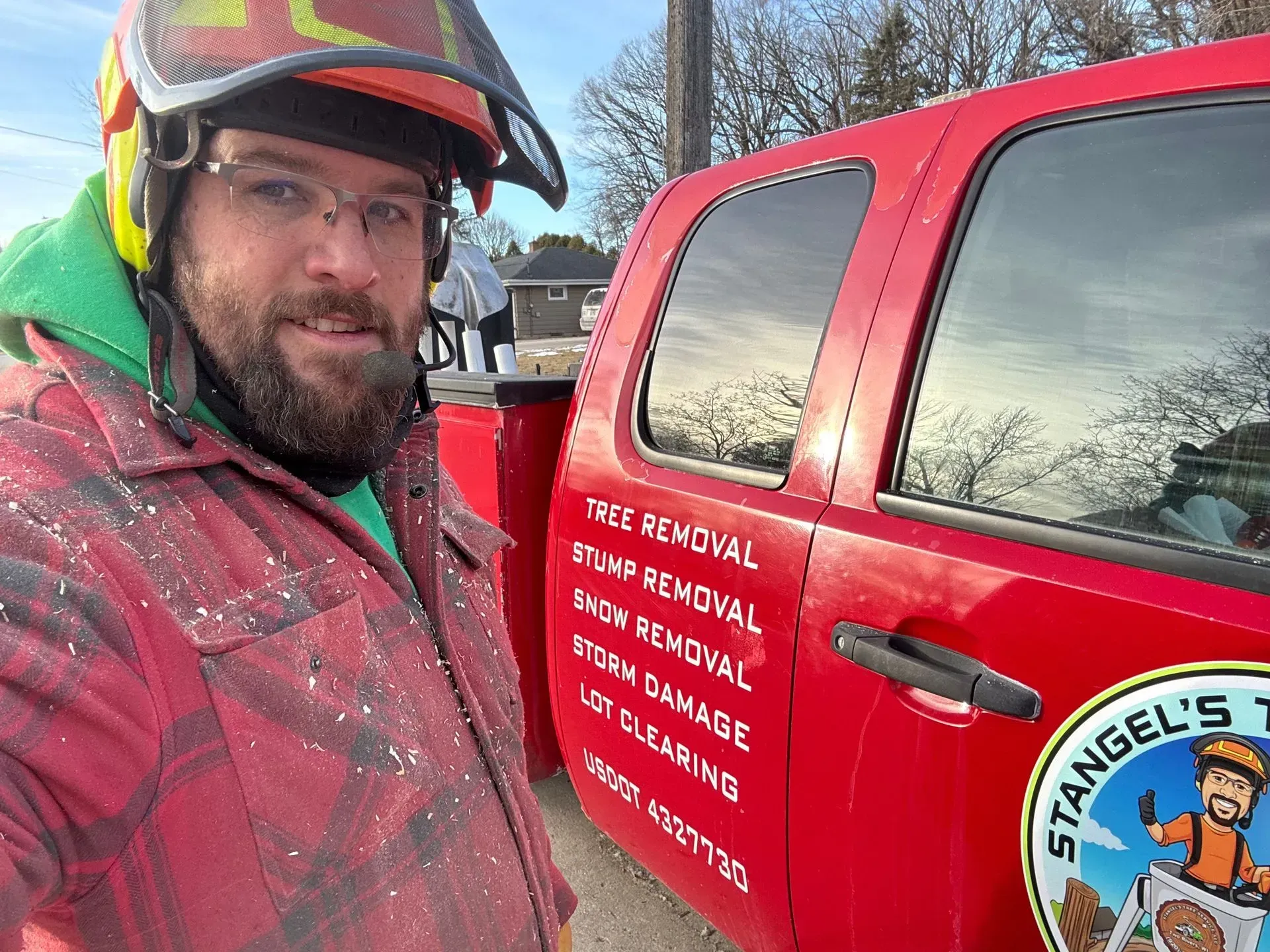 Worker in helmet and safety glasses beside a red service truck with company logo in snowy weather