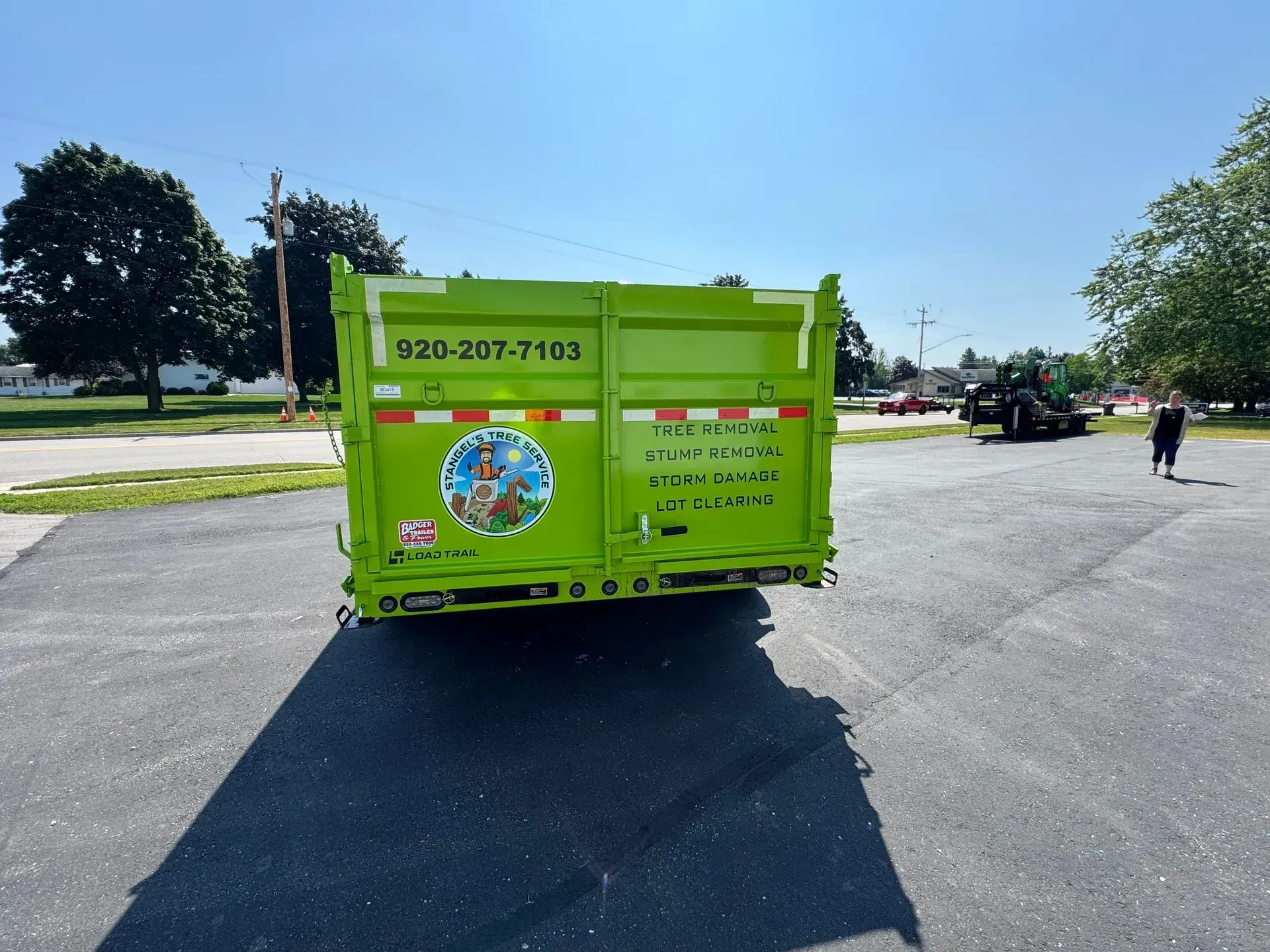 Bright green dumpster trailer in a parking lot with trees and a person in the distance