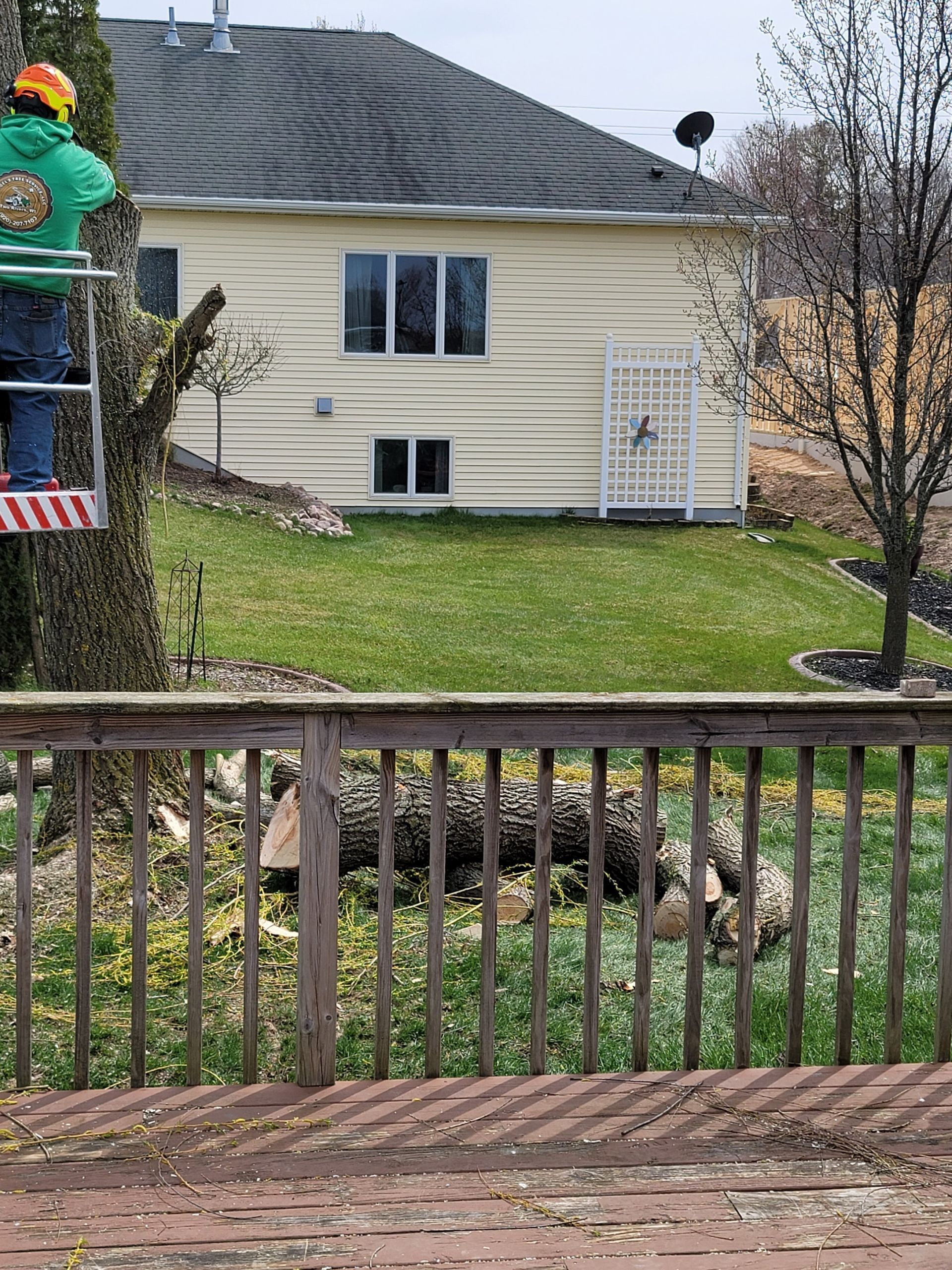 Backyard view of beige house with dark roof, green lawn, and wooden deck railing in the foreground