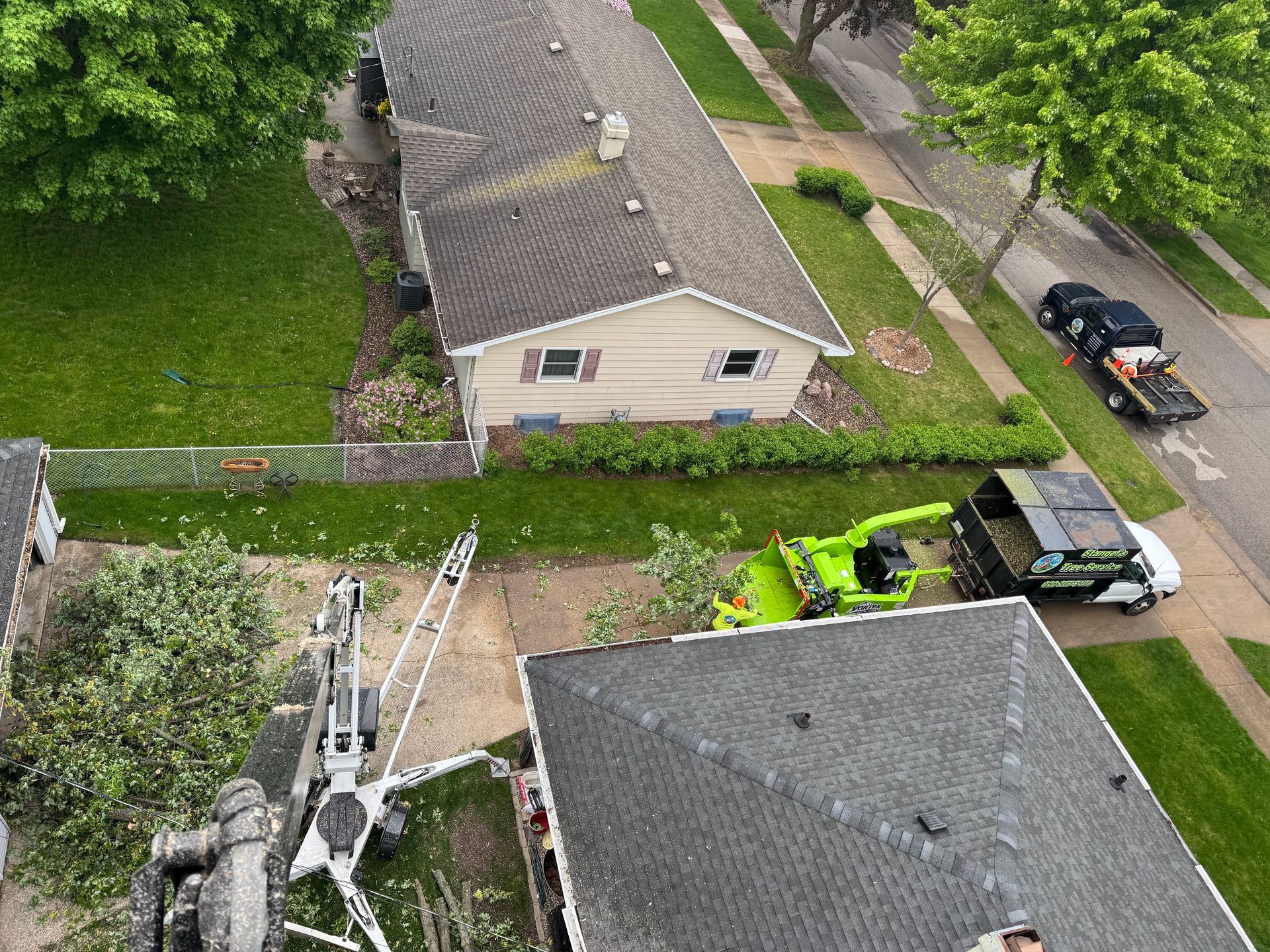 Aerial view of a house roof with a green excavator and a black truck in a yard.