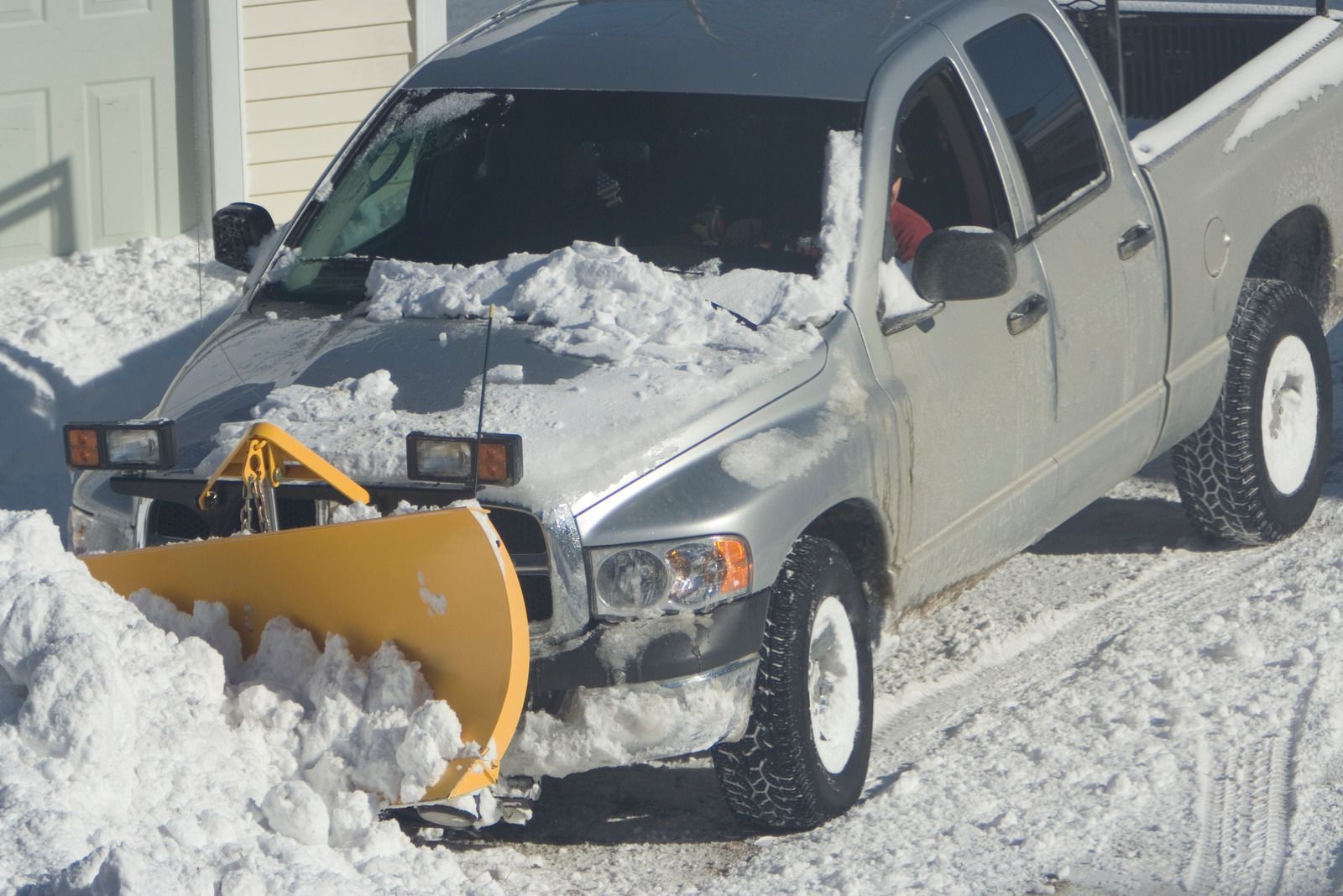 Silver pickup truck with a yellow snowplow pushing snow in a snowy driveway