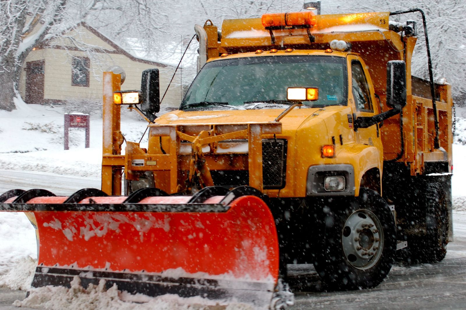Yellow snowplow clearing a snowy street in front of houses
