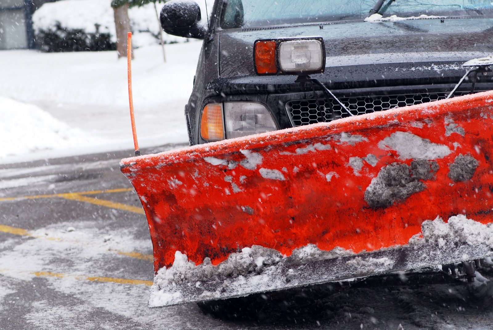 Snowplow blade clearing a snowy road beside a black truck