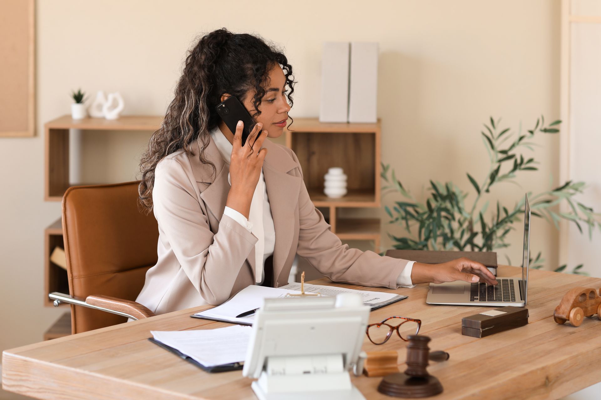 A woman is sitting at a desk talking on a cell phone.