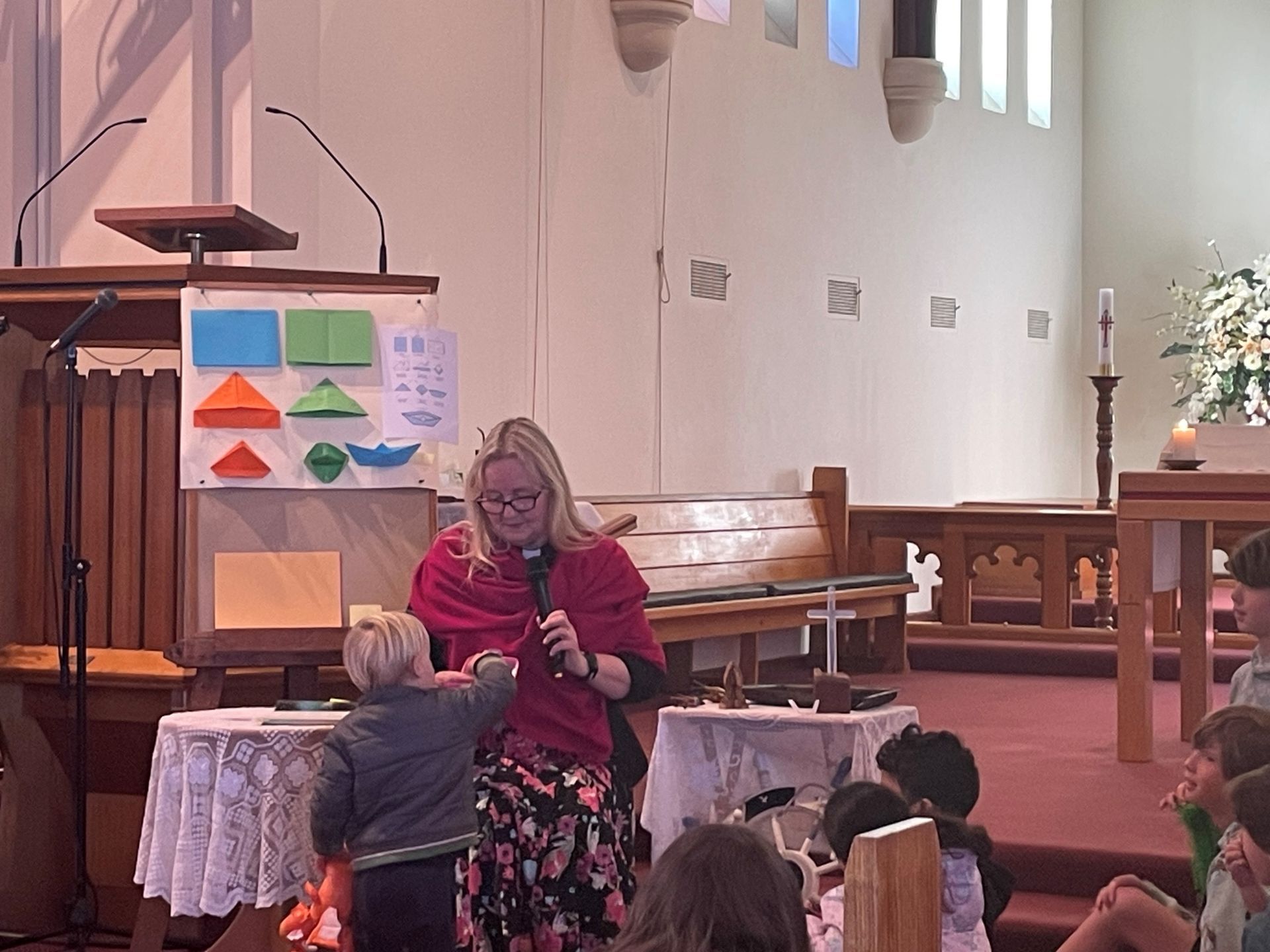 A priest is giving a Kid's Talk to a group of children in a church.