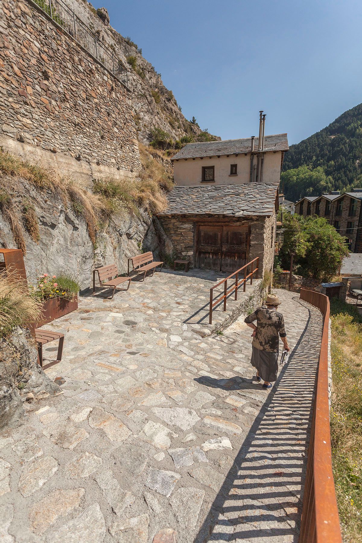 Una mujer camina por un camino de piedra hacia un edificio. Fotografia Emfasi Estudi Andorra y Barcelona.