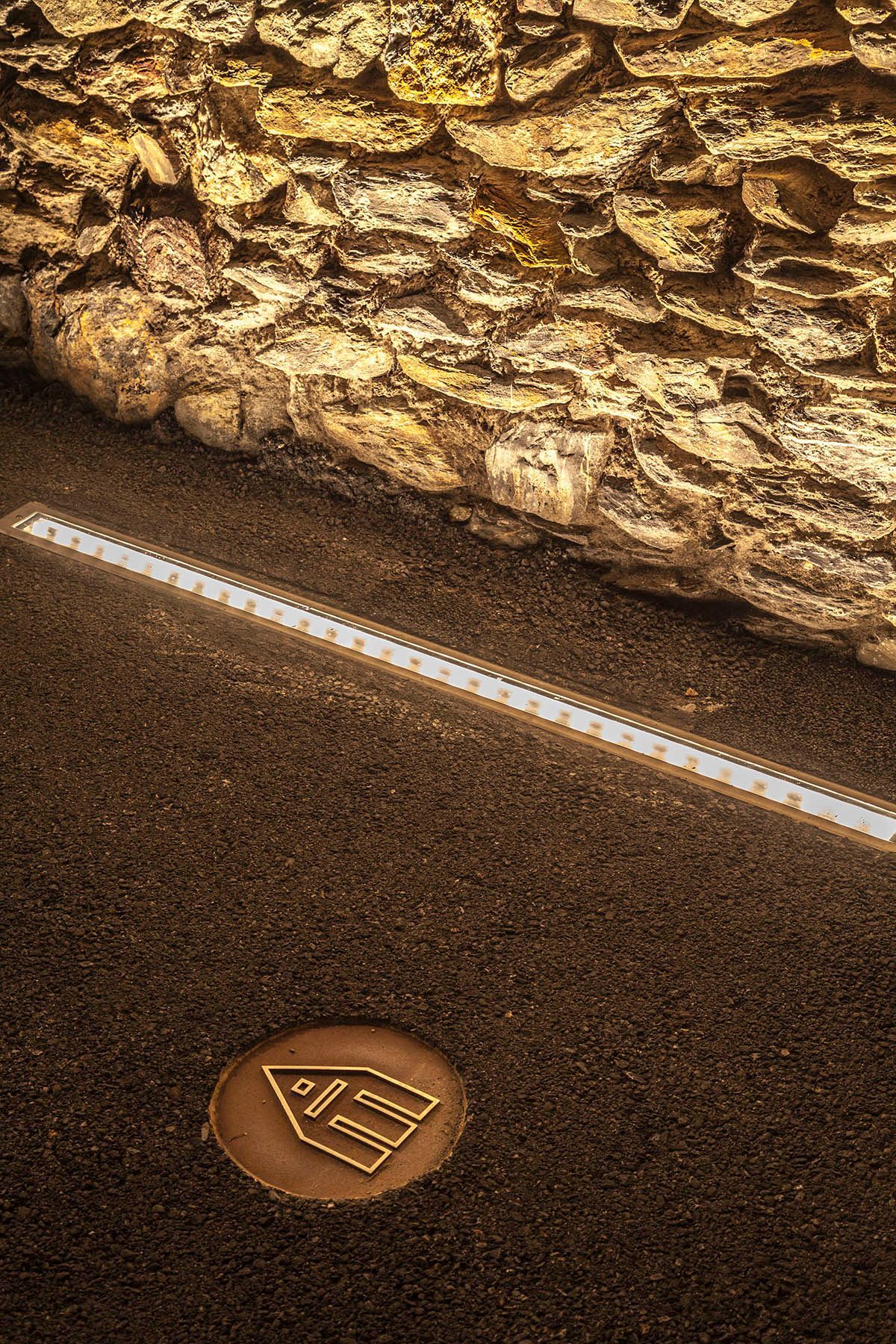 Hay un muro de piedra al fondo y unas luces led en el suelo. Emfasi Estudi